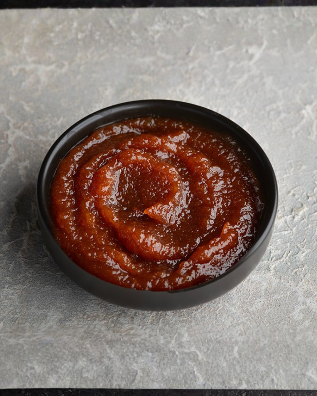 Black bowl filled with Amla Chutney sauce on a gray surface