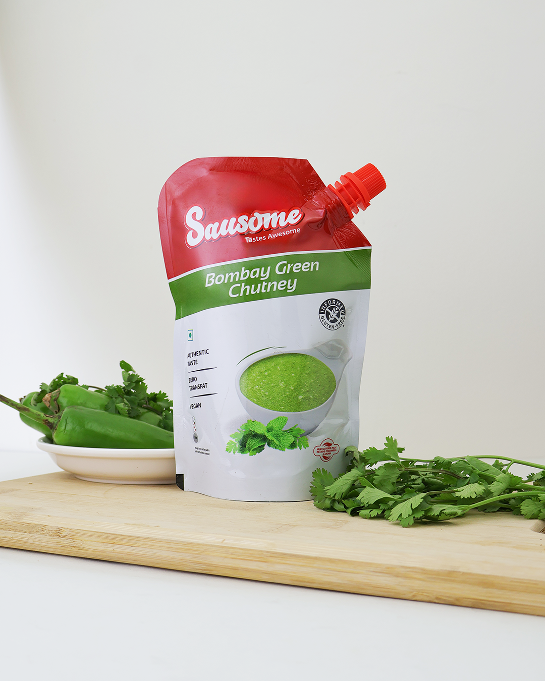 Sausome Bombay Green Chutney packaging on a wooden board with green chilies and coriander leaves.