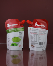 Two Sausome Bombay Green Chutney packets on a reflective surface with a dark background