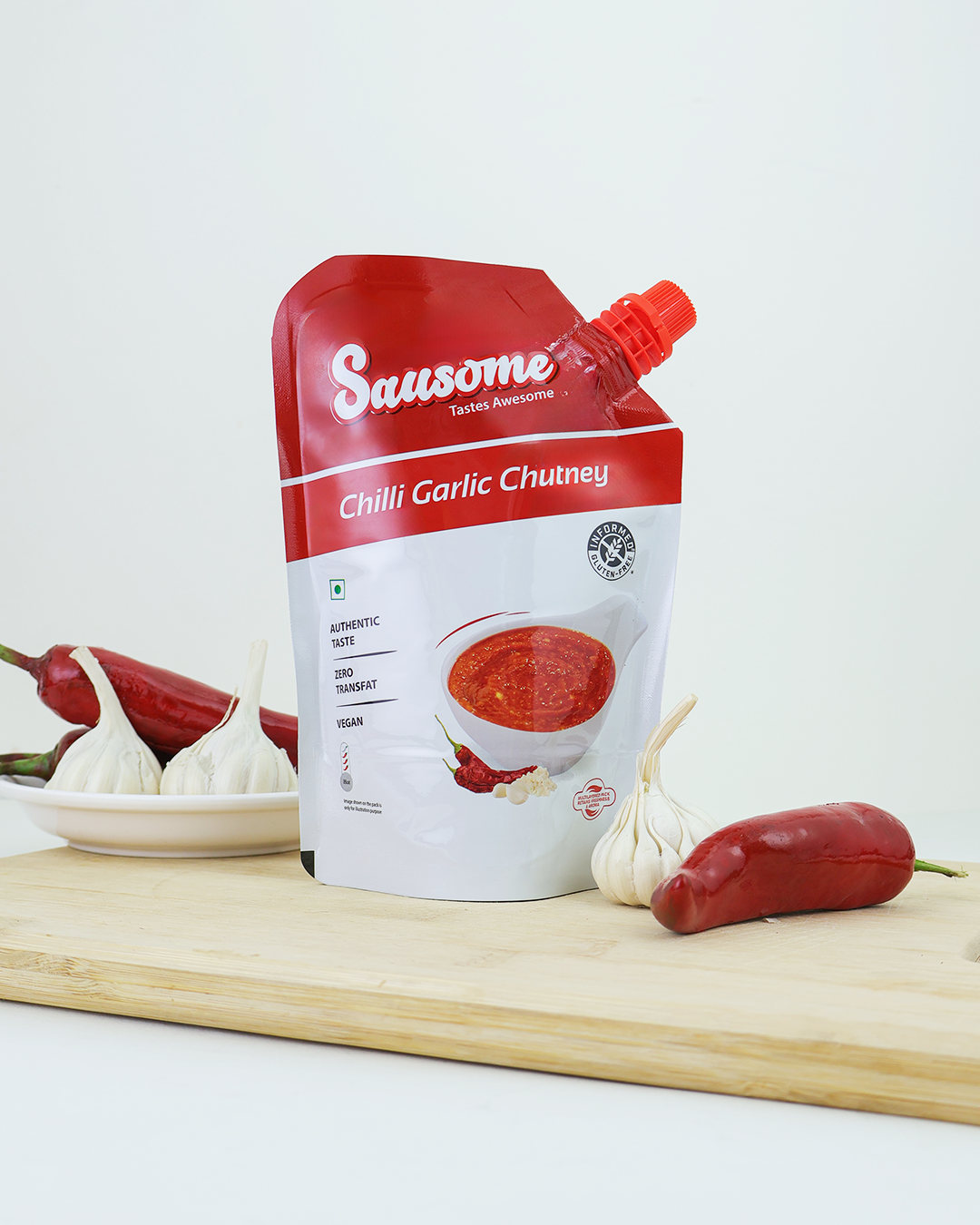 Sausome Chilli Garlic Chutney packaging on a wooden board with chilies and garlic.