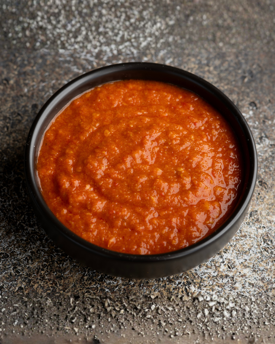 Black bowl filled with Chilli Garlic Chutney on a textured gray surface
