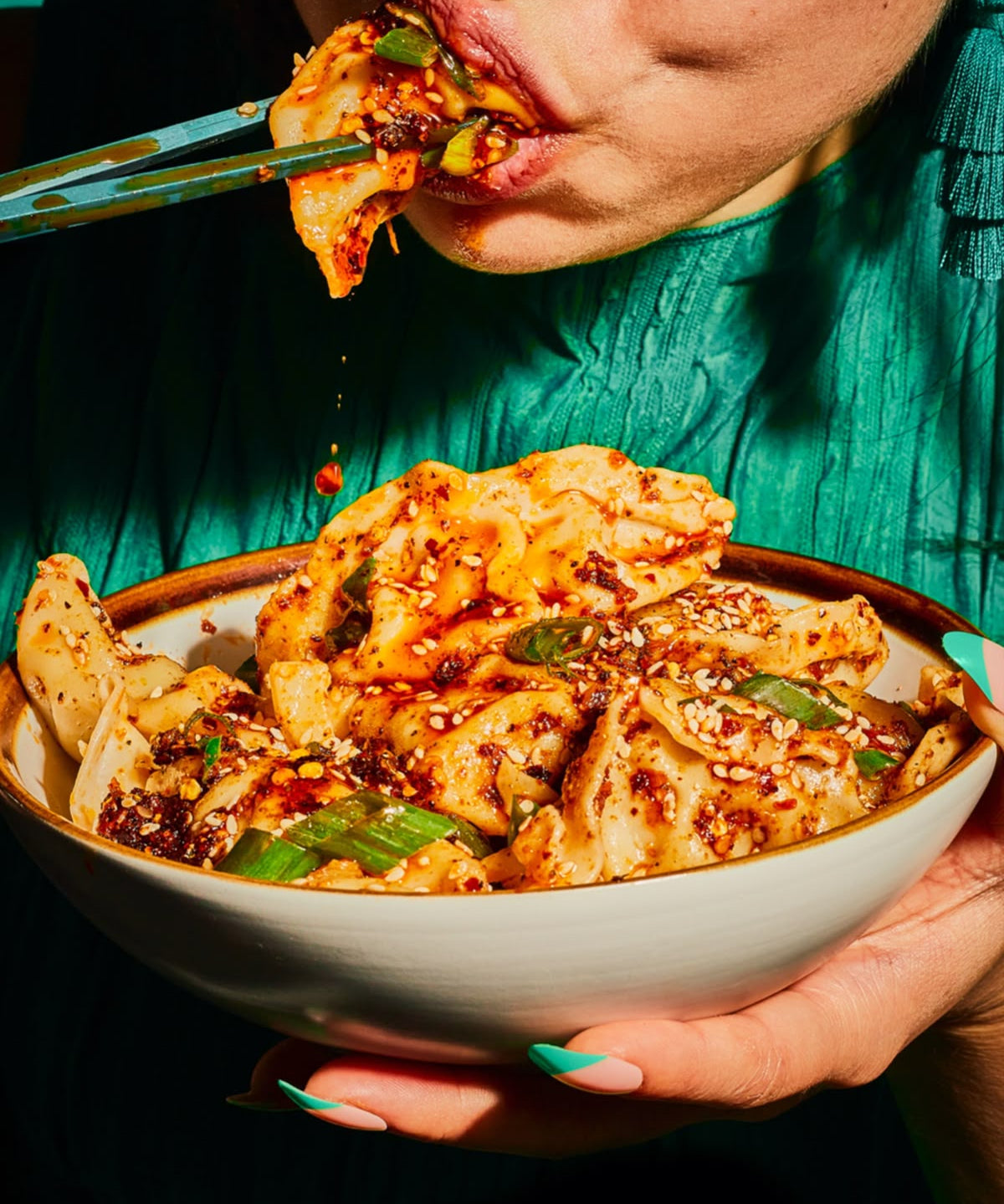 Person eating a bowl of spicy noodles with a fork, wearing a green shirt.