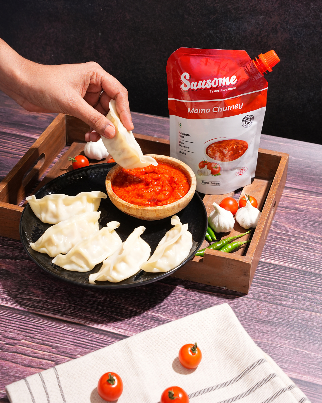 Person dipping a Momo into a bowl of  Sausome momo chutney packet on a wooden tray.
