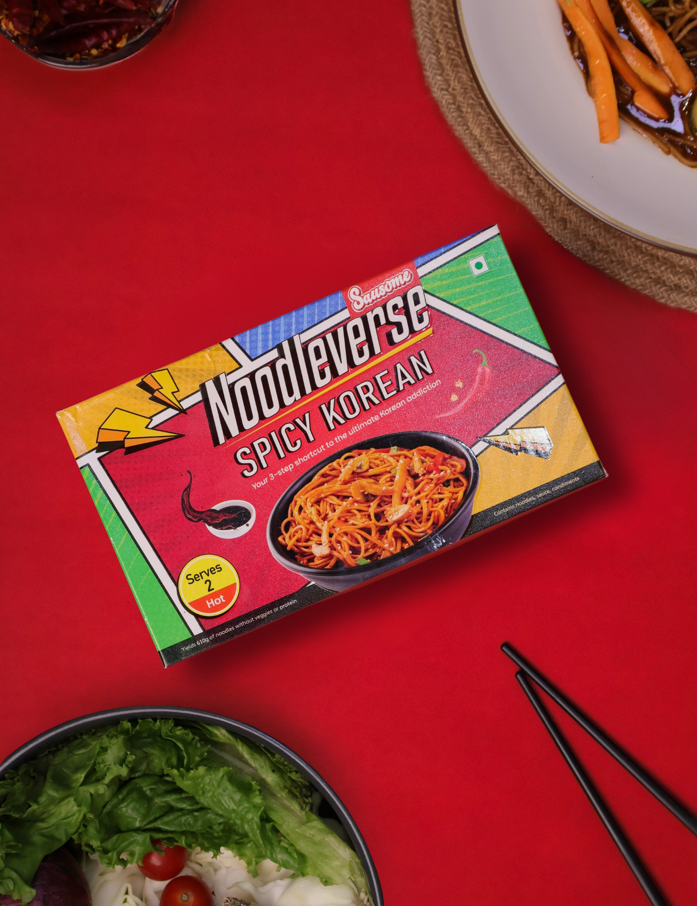 Noodleverse Spicy Korean noodle box on a red background with a salad and chopsticks.