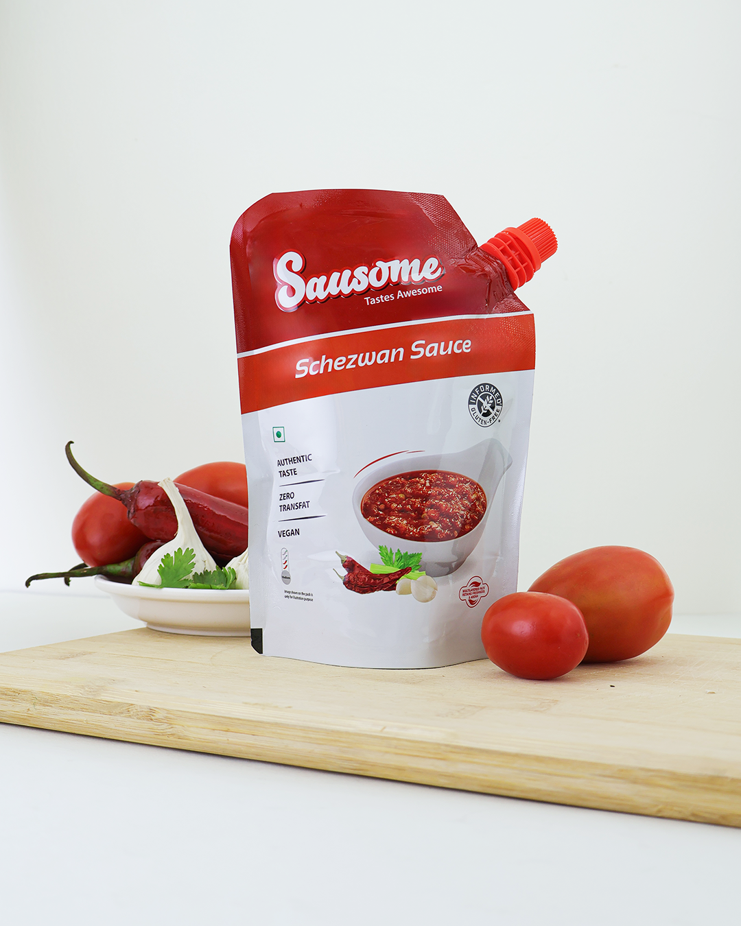 Sausome Schezwan Sauce packaging on a wooden board with tomatoes and chilies.