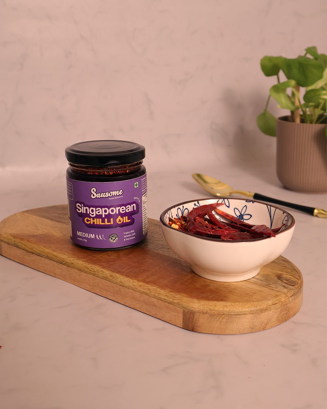 Jar of Singaporean Chilli Oil on a wooden board with a bowl of dried red chilies.
