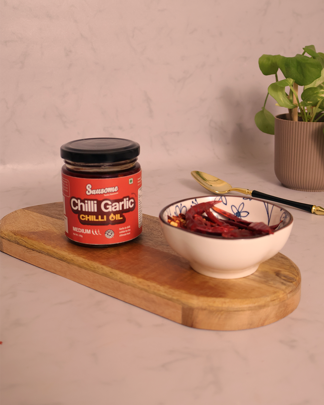 Jar of Red Chilli Garlic Chilli Oil on a wooden board with a bowl of dried red chilies.